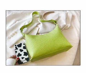 Detailansicht der neongrünen Tasche mit Litschi-Maserung und Knotengurt auf weißem Blazer