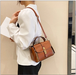 Dettaglio borsa a mano in pelle marrone con chiusura dorata su blazer bianco
