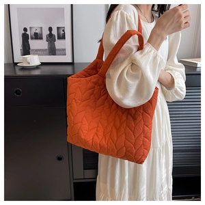 Detailansicht der orangen Stepptasche mit Blattmuster-Nähten und breitem Gurt