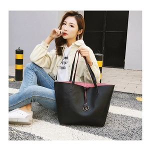 Detail of black pebbled leather tote bag with red lining and golden ring accents