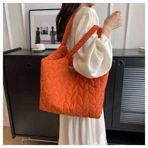 Detail der orangefarbenen gesteppten Puffertasche mit Blattmuster und breitem Trageriemen