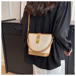 Detail view of woven bucket bag with brown leather trim and golden metal clasp on a model