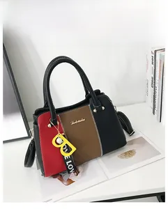 Détail d'un sac cabas bicolore en cuir grainé avec pendentif jaune sur bureau blanc