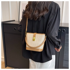 Detail of herringbone straw bucket bag with brown leather handle and metal lock clasp