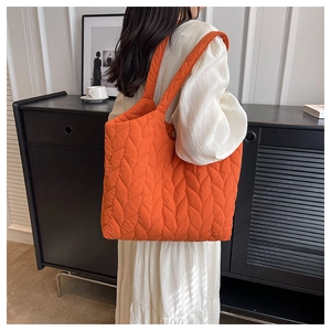 Detailansicht einer orangefarbenen Stepptasche mit Blattadermuster und breitem Gurt
