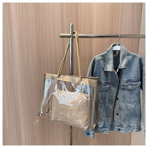 Detail of transparent PVC tote bag featuring gold rope handles and inner cloth pouch