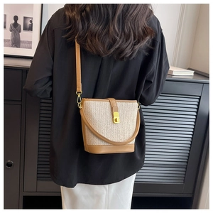 Detail of woven straw bucket bag with brown leather trim and golden metal twist lock