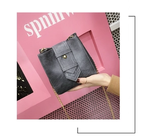 Close-up of grey crossbody bucket bag with gold studs and delicate metal chain strap