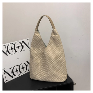 Detailansicht der beigen Stepptasche mit braunen Ledergriffen und Quadratstruktur