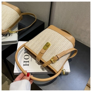 Close-up of woven straw bucket bag featuring brown leather trim and golden metal lock