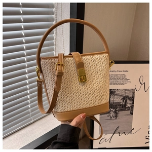 Detail of large straw bucket bag with brown leather strap and golden metal clasp