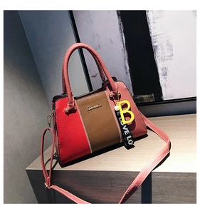 Détail d'un sac à main tricolore en cuir avec breloque lettre B et sangle tissée