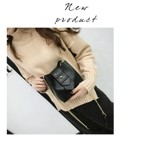 Detail view of black mini crossbody bag with gold chain strap and V-shaped clasp on sweater
