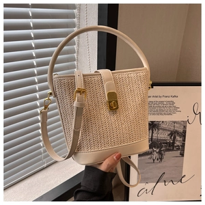 Detail of a beige woven straw bucket bag with leather handles and a gold twist-lock