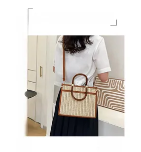 Detail of hand-woven straw tote with brown leather trim and round retro handles