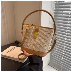 Detail of bohemian straw bucket bag with brown leather trim and golden metal lock