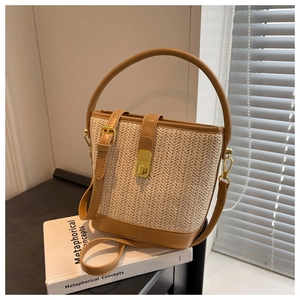 Detail of woven straw bucket bag with brown leather trim and golden metal lock