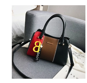 Détail du sac à main tricolore en cuir grainé avec pendentif B jaune sur un canapé gris