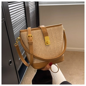 Close-up of straw bucket bag featuring brown leather trim and golden metal swivel lock