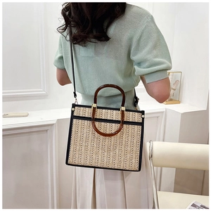 Detail view of woven straw tote bag featuring black trim and amber resin ring handles
