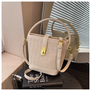 Detail of beige woven bucket bag with leather stitching and gold metal twist lock
