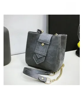 Detail view of a gray bucket bag with white stitching and golden metal hardware details