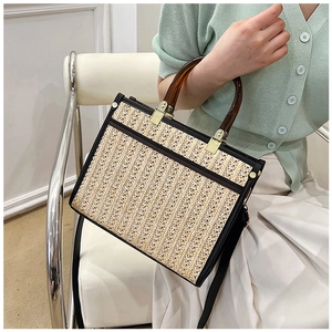 Detail of hand-woven straw tote with amber acrylic handles and black leather trim