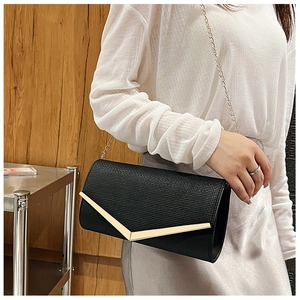 Detail showing the elegant black envelope clutch bag with gold V-shaped metal trim