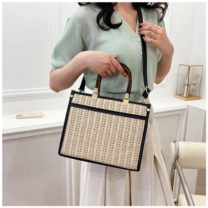 Detailed view of handmade beige woven tote bag with amber texture handles and black leather trim