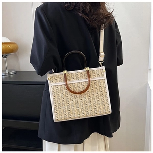 Detail view of woven straw tote bag with dual-tone ring handles and leather strap