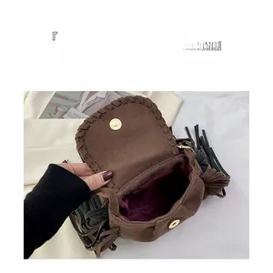 Detail view of brown suede saddle bag with woven edges, tassel and large interior storage