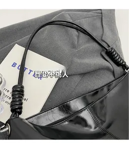 Detail of glossy black pleated leather bag with unique thick knotted shoulder strap