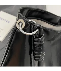 Close-up of black glossy leather bag showing silver metal ring and knotted strap detail