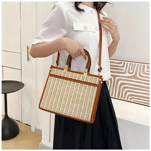 Detail of straw tote bag with brown leather trim and acrylic handles on model