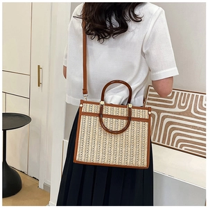 Detail view of woven straw tote bag with brown leather handles and shoulder strap
