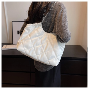 Detailed view of white quilted tote bag with silver chain strap worn by a model