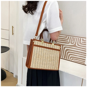 Detail of beige woven tote bag with brown leather handles worn by a model in a room