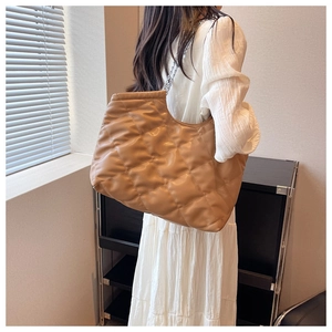 Detailed view of caramel quilted tote bag featuring silver chain straps on model