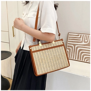 Straw tote bag detail showing brown leather straps and woven texture on a model