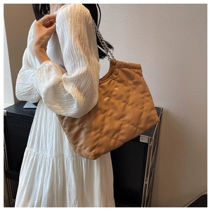 Side view of a brown quilted tote bag with silver chain strap worn by a model