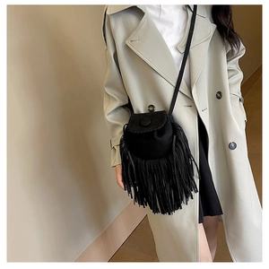 Close-up of black suede saddle bag with long tassels and woven stitching details