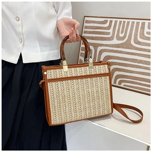 Detail of straw tote bag with amber resin handles and brown leather trim on a model