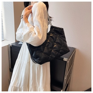 Detailed close-up of a large black quilted tote bag with silver chain straps on a model