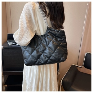 Close-up of black quilted tote bag with silver chain strap worn by model in white dress