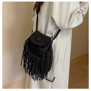 Detail of black suede saddle bag with dense fringes and round buckle on a light trench coat