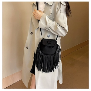 Detail view of a black suede crossbody saddle bag with long tassels on a beige trench coat