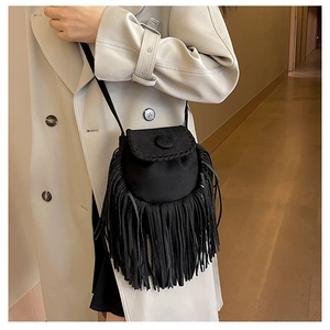 Detail of a black suede tassel saddle bag worn with a coat in a stylish indoor setting