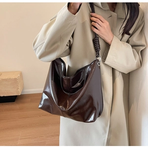 Detail of glossy dark brown leather shoulder bag with decorative strap knot and silver ring