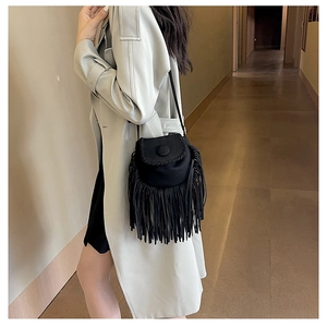 Close-up of a black faux suede saddle bag with long fringe detailing and slender strap