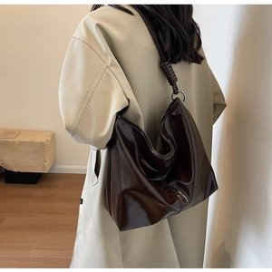 Detail of dark brown tote bag featuring glossy texture and decorative knot on shoulder strap